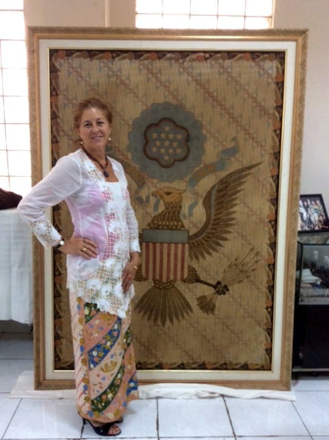 Julia standing beside a framed textile banner featuring an eagle emblem during her return visit to Jakarta.