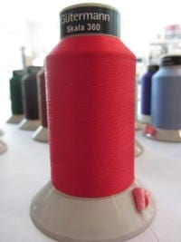 A large red polyester thread spool, with additional thread spools visible behind.