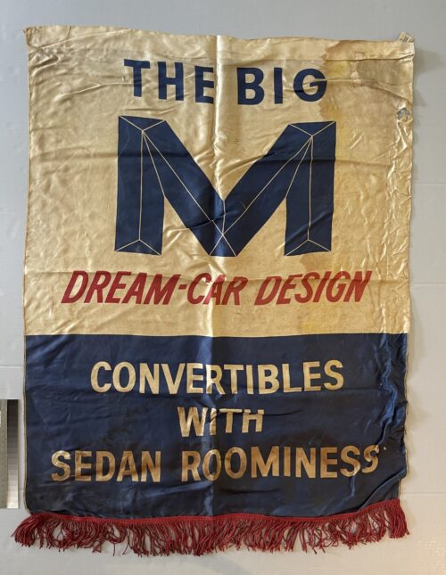 Vertical printed fabric banner advertising “The Big M Dream-Car Design,” with blue and red lettering and a red fringe along the bottom edge.