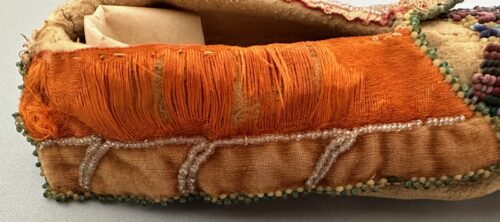 Native American slipper showing orange textile trim and beadwork along the sole.