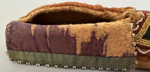 Side view of Native American slipper after treatment, showing stabilized textile and bead edging.