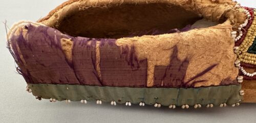 Side view of beaded Native American slipper showing worn textile and bead edging.