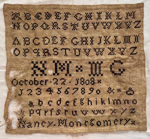 Rectangular linen sampler embroidered with rows of upper- and lowercase alphabets, numerals, decorative initials, and a stitched date reading “October 22, 1808,” laid flat before treatment.