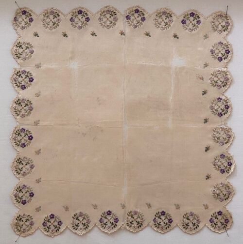 Square white silk handkerchief laid flat before treatment, featuring scalloped edges and delicate embroidered floral clusters in purple, and green along the border.