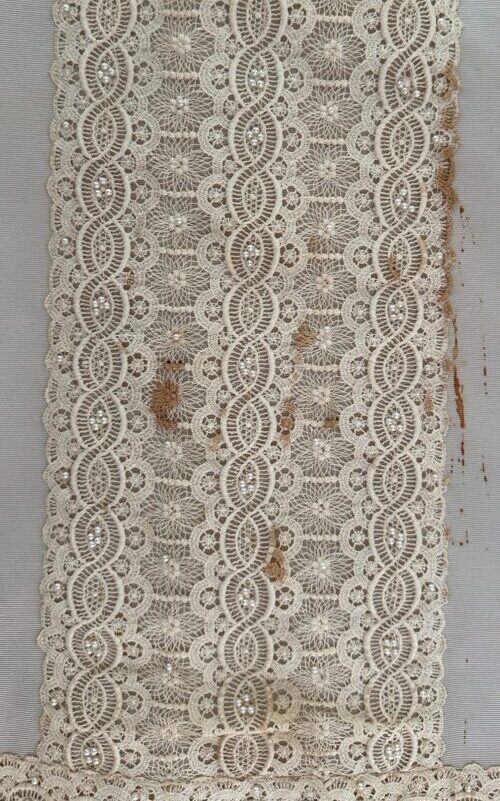 Wedding dress lace detail before treatment showing discoloration and stains, photographed flat against a neutral support.
