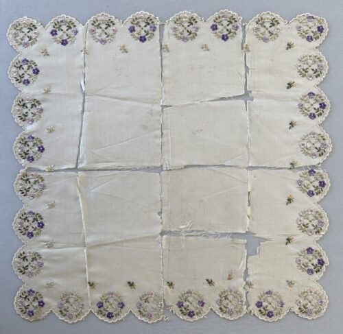 Square white silk handkerchief after treatment, featuring scalloped edges and delicate embroidered floral clusters in purple, and green along the border.