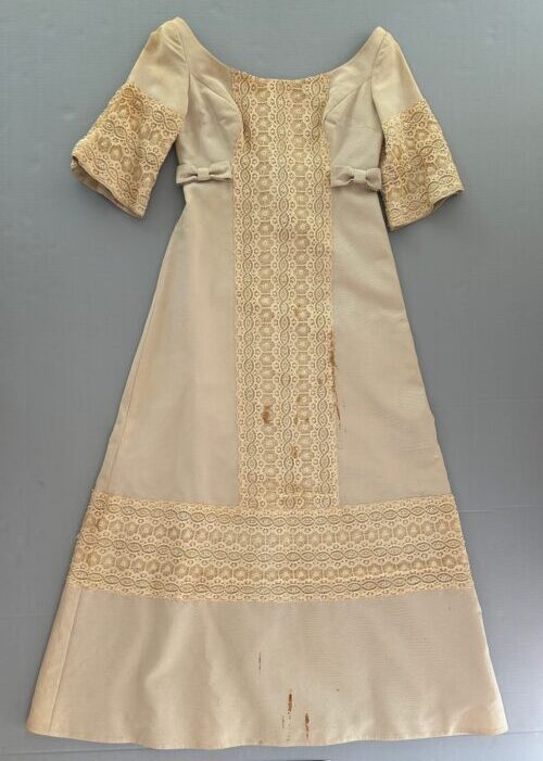 Wedding silk dress in cream color with lace panel and short sleeves before treatment showing discoloration and stains, photographed flat against a neutral support.