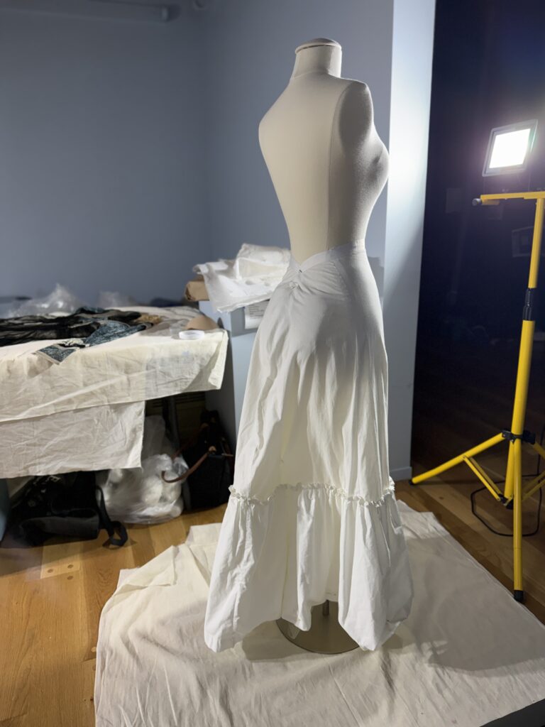 Standing female dress form, seen from back, with long cream-colored slip skirt from waist to floor.