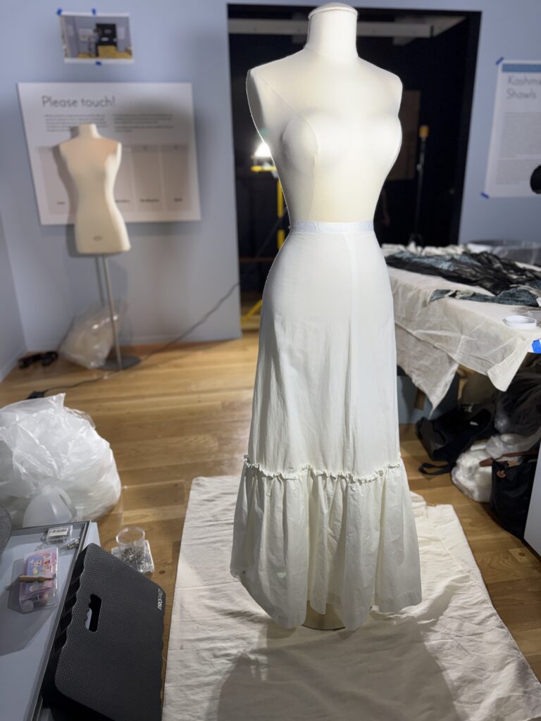 Standing female dress form, seen from front, with long cream-colored slip skirt from waist to floor.