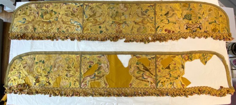 Two pieces of long horizontal shaped gold colored shiny cloth covered in floral embroidery and outlined with yellow borders. The top one is complete. The bottom one has large white holes in the center and left side.