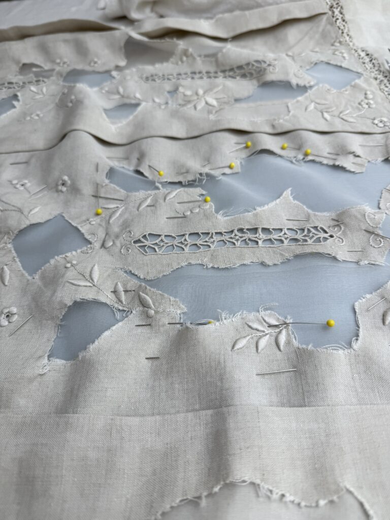 The same cream-colored linen cloth flattened out with a sheer invisible fabric in the holes, pinned with yellow headed straight pins.
