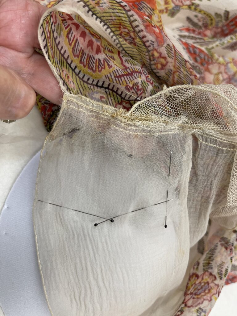 Close up of silk paisley dress and white silk chiffon fabric with pins securing a stitching repair.