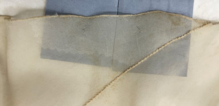 Close up of white silk chiffon fabric and repair fabric behind it on a grey board.