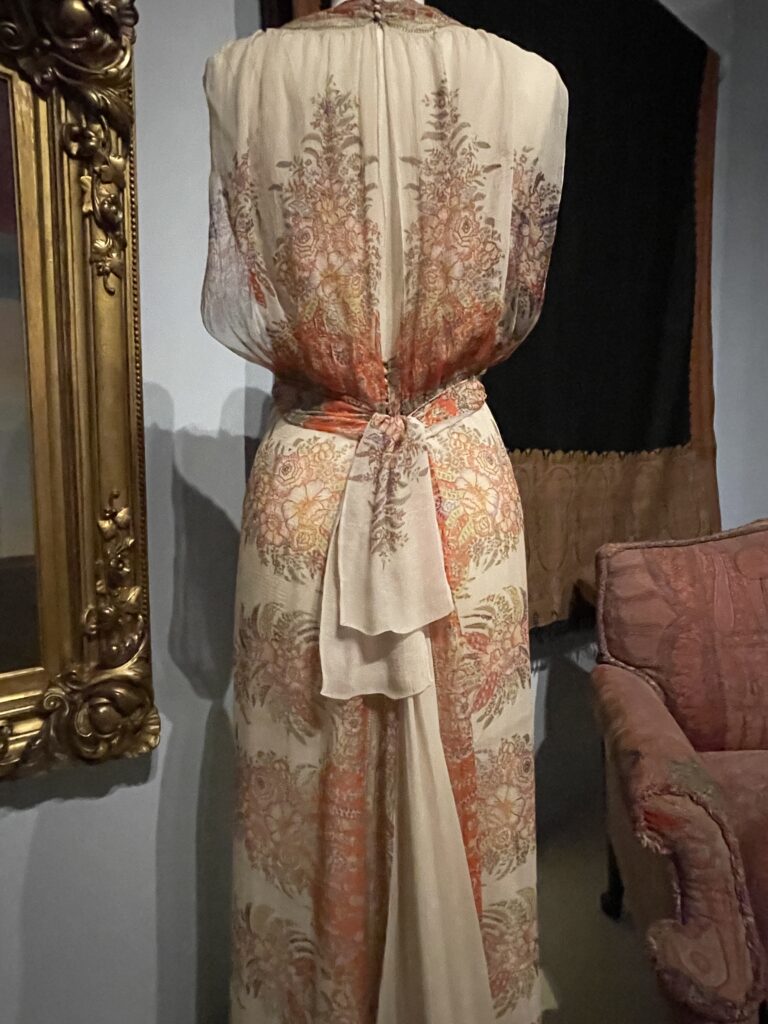 Detail of cream colored and pink long dress with tie in back, showing pattern of curvilinear patterns known as paisley.
