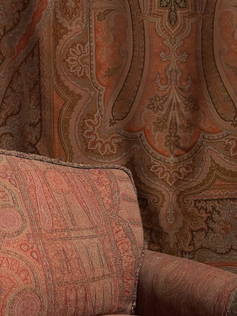 Close up of red colored sofa and cloth on wall with curving patterns known as paisley.