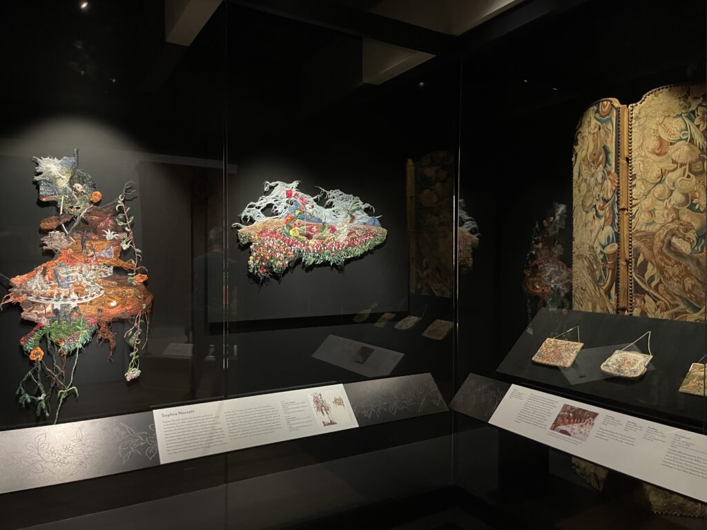 Dark room with black walls with three textiles illuminated on display.