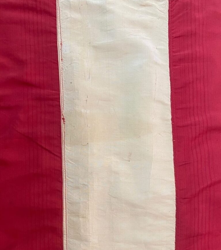 Detail of long narrow vertical white shiny silk strip on red background, smooth and with no tears or wrinkles.
