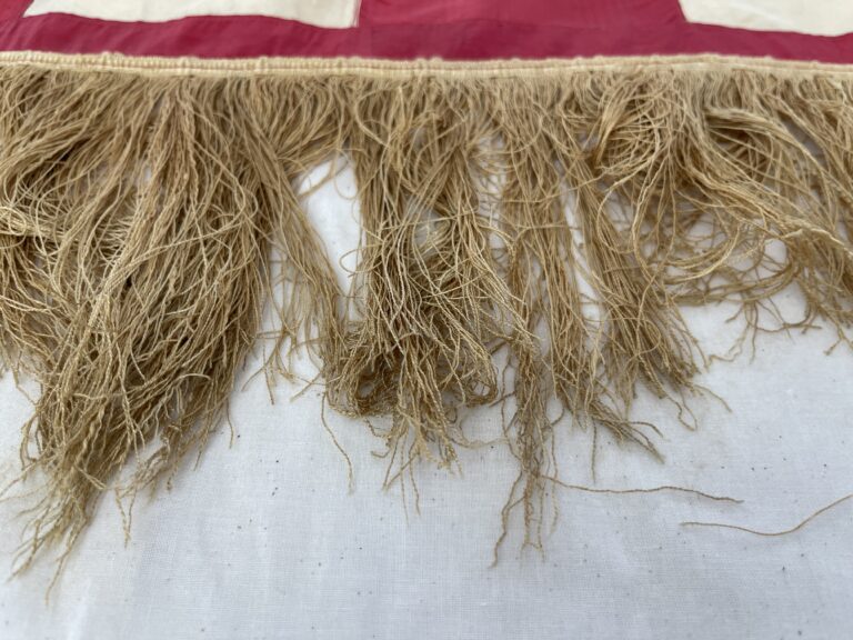 Tangled gold fringe at bottom edge of a red textile edge.
