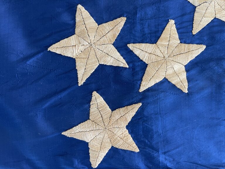Close up of white embroidered stars on shiny blue silk fabric.