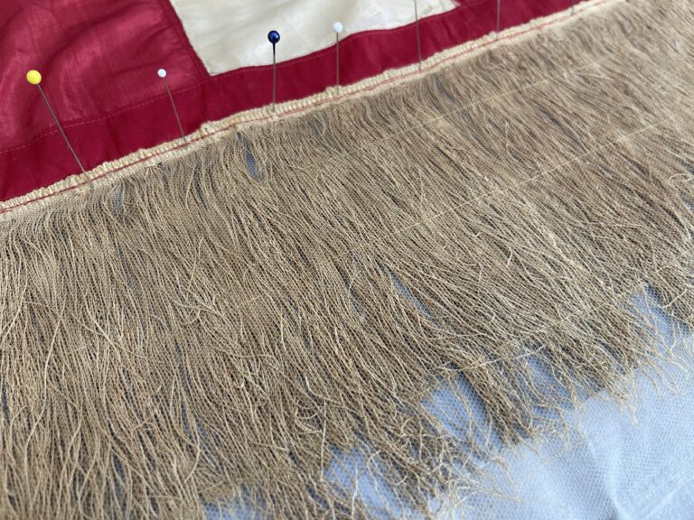 Gold-colored threads laid out smoothly and straight, along the edge of the red and white stripes of the flag.