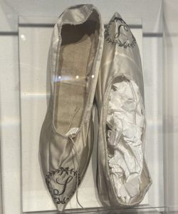 Mother Seton's ivory silk slippers displayed upright in a glass museum case.