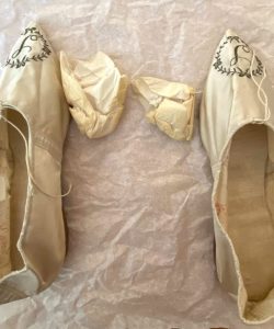 Mother Seton's ivory silk slippers with pointed toes and embroidered monograms laid flat on tissue paper with removed stuffing.