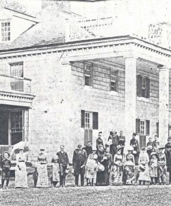 Photo of Frederick Douglass's large, stately, white columned home with balconies, surrounded by visitors.