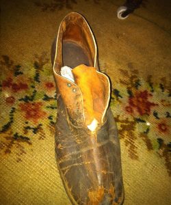 Badly worn single, brown leather shoe set on needlepoint rug, worn by Frederick Douglass