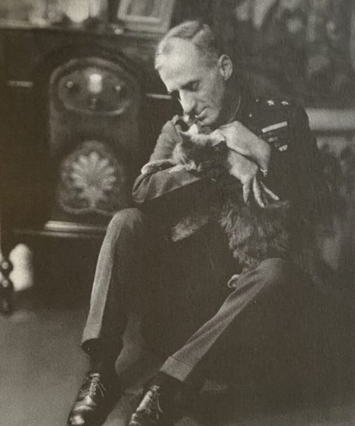 Black-and-white photograph of Smedley Butler seated in uniform, leaning forward while holding and looking at a small dog in his arms.