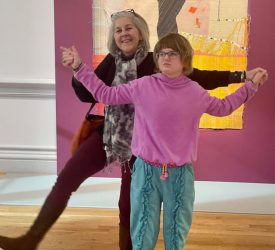 Julia and young girl pose in front of a large textile artwork in a museum gallery.
