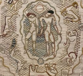 An embroidered textile featuring an ornate central monogram surrounded by stitched animal and decorative flourishes.
