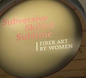 Gallery entrance signage displaying the exhibition title Subversive Skilled Sublime: Fiber Art by Women within a large circular wall graphic.