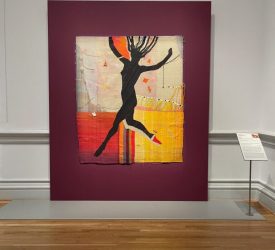 Textile artwork featuring silhouetted figure mounted on plum-colored wall.
