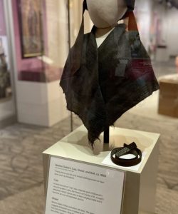 Mother Seton's black bonnet and dark shawl mounted on a mannequin head and bust, displayed in a glass museum case with interpretive label beneath.