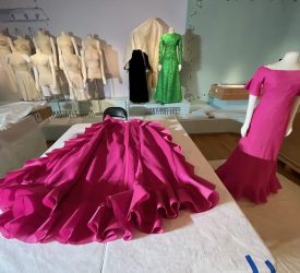 Bright fuchsia gown from Princess Grace Kelly's collection laid out for mounting beside matching dress on mannequin during exhibition installation.