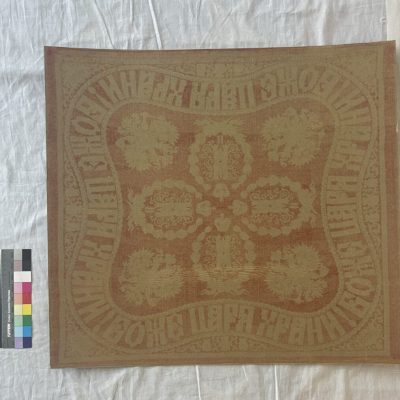 Brown cardboard with very faint design of a textile on it, and grey and multi colored photo color card on the left.