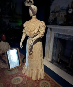 Mannequin dressed in an embroidered historic gown displayed in a period-style interior.