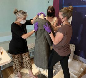 Julia and her colleagues carefully position a gray textured dress on a mannequin in a gallery space.