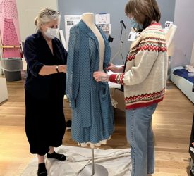 Julia and her colleague carefully adjust a blue patterned dress on a mannequin during exhibition installation.