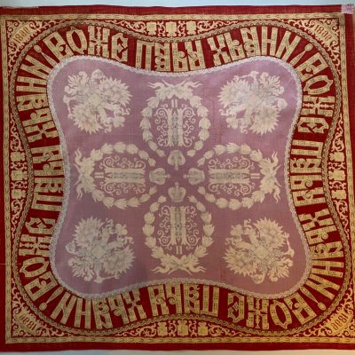 Red and cream-colored printed cloth handkerchief, with pale white sheer cloth over the middle of textile.