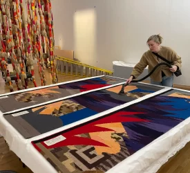 Textile conservator vacuuming large textile panels during gallery installation.