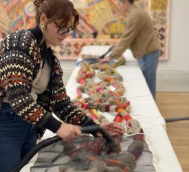 Textile conservators vacuuming textile cords through protective screen during installation.