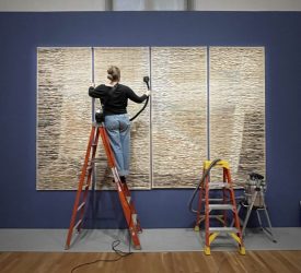 Textile conservator vacuuming large wall-mounted textile panels during installation.