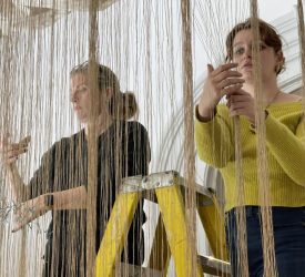 Two textile conservationists adjusting suspended fiber installation during gallery setup.