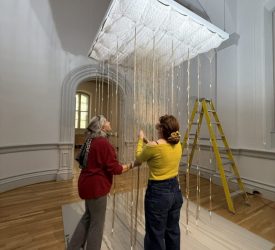 Julia and colleague installing suspended fiber artwork in gallery space.