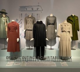 Mannequins display tailored coats, suits, and day dresses worn by Princess Grace Kelly. The garments are arranged on tiered platforms beneath the exhibition heading “Official Outings & Charitable Work.”