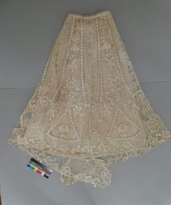Full view of a historic cream-colored lace skirt laid flat after conservation treatment.
