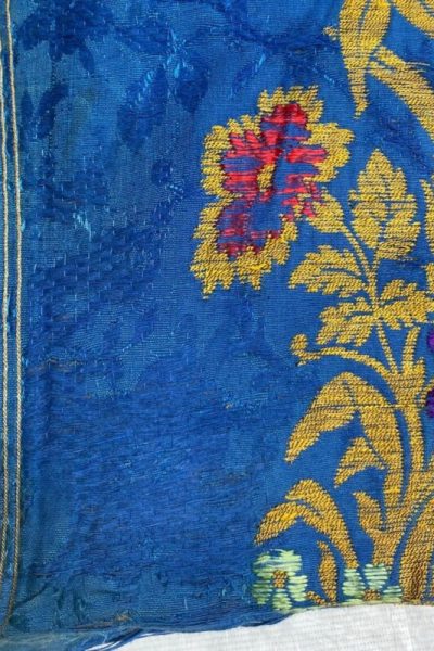 Repaired weft threading of damask fabric with vibrant blue background and golden floral along right side