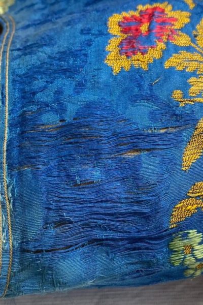 Damaged, abraded damask fabric with vibrant blue background and golden floral along right side