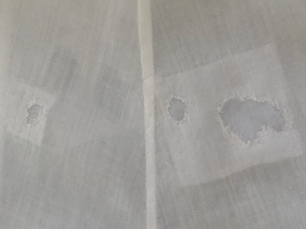 White linen fabric with hole, repaired with couching stitches.